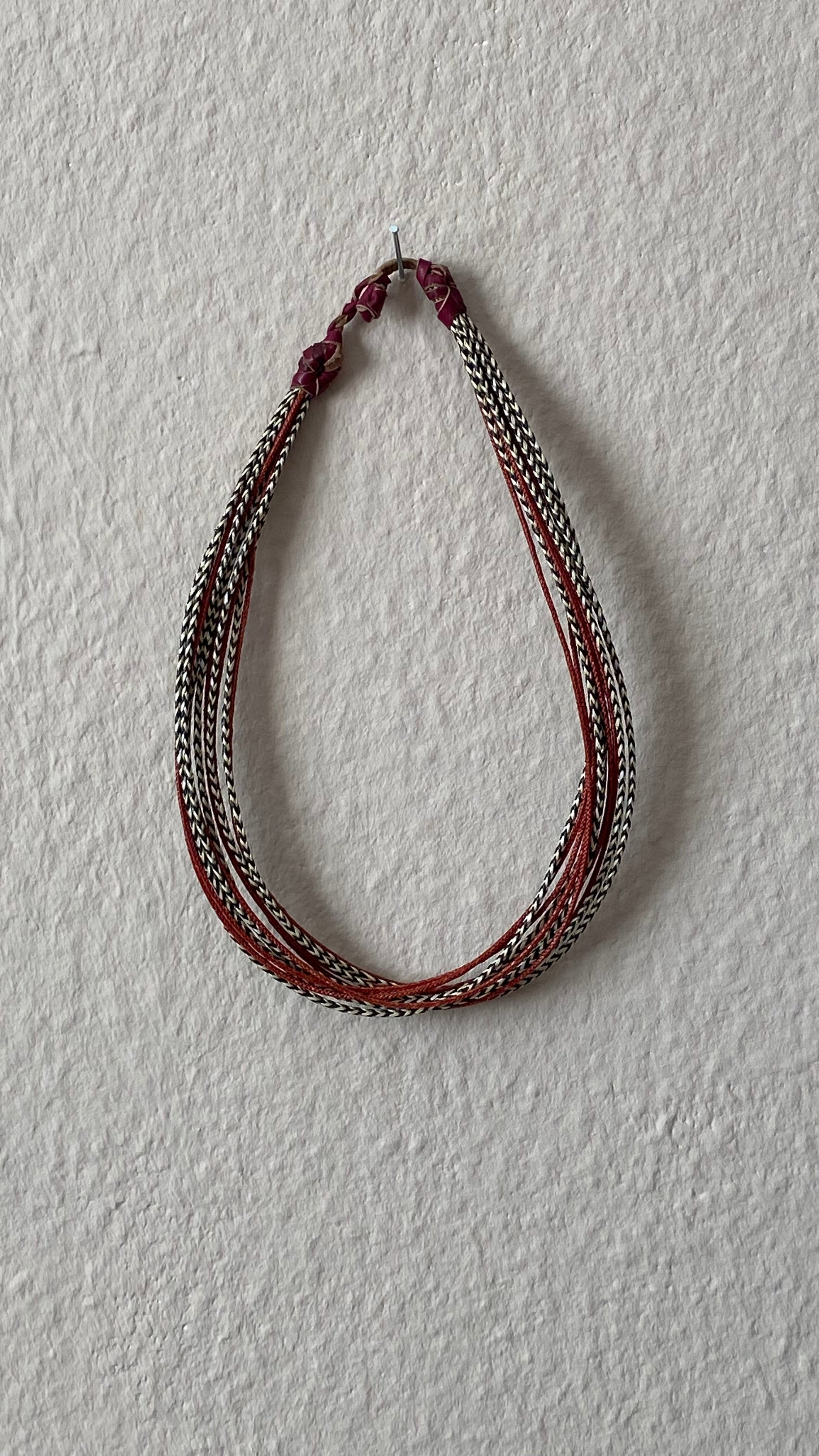 Moumi Halskette von ABENIN – handgefertigter Grasschmuck in harmonischer Flechtung aus rotem, schwarzem und naturfarbenem Gras. Mit Lederabschluss – nachhaltig, fair produziert und voller Charakter.