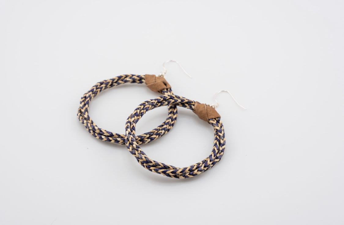 Sota Ohrringe von ABENIN – handgefertigte Creolen aus geflochtenem Naturgras in Dunkelblau und Beige mit Lederdetail. Fair produziert, nachhaltig und stilvoll.