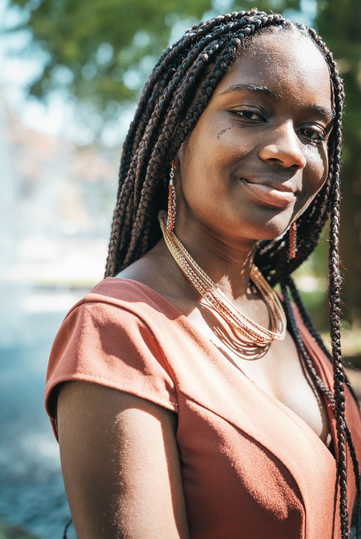 Frau mit ABENIN Zou Ohrringen und der Moumi Halskette – handgefertigter Schmuck aus Benin aus Pflanzenfasern und Perlen, stilvoll getragen in der Sonne.